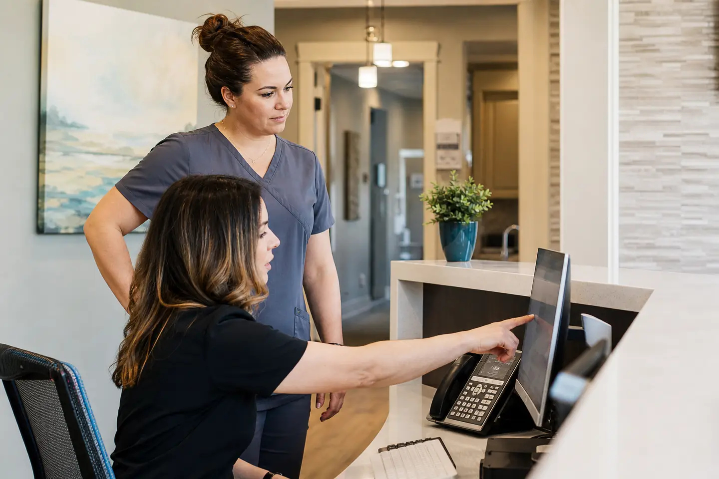 A dental front-desk coordinator finding an approved answer while a coworker waits nearby